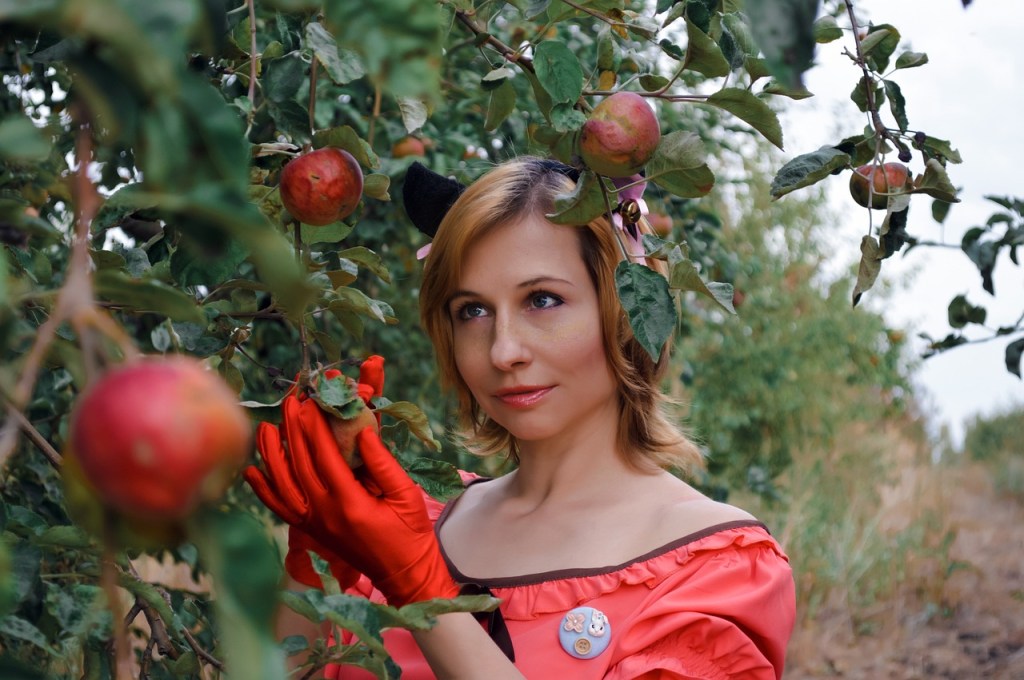 a woman in a red dress picks red apples